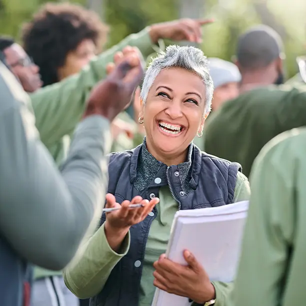 A smiling woman holding a stack of papers amongst a light crowd of people