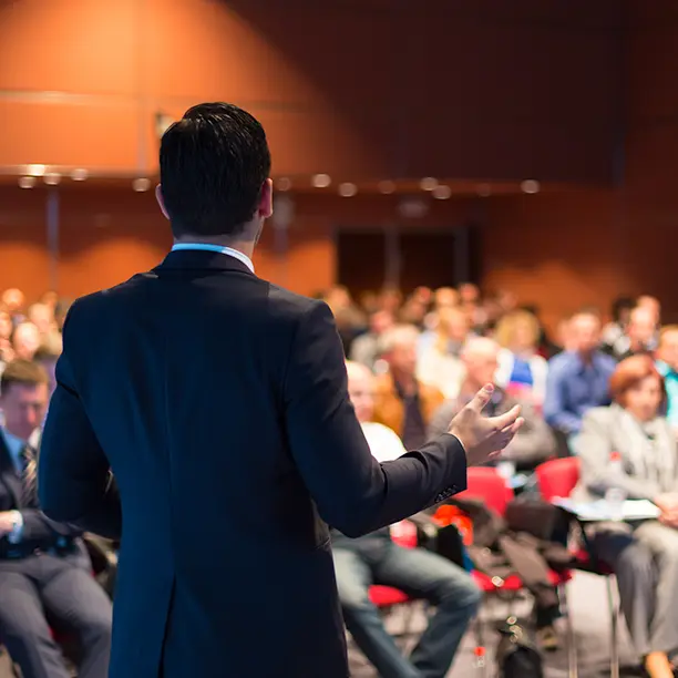 A man in a suit speaks to a room full of people